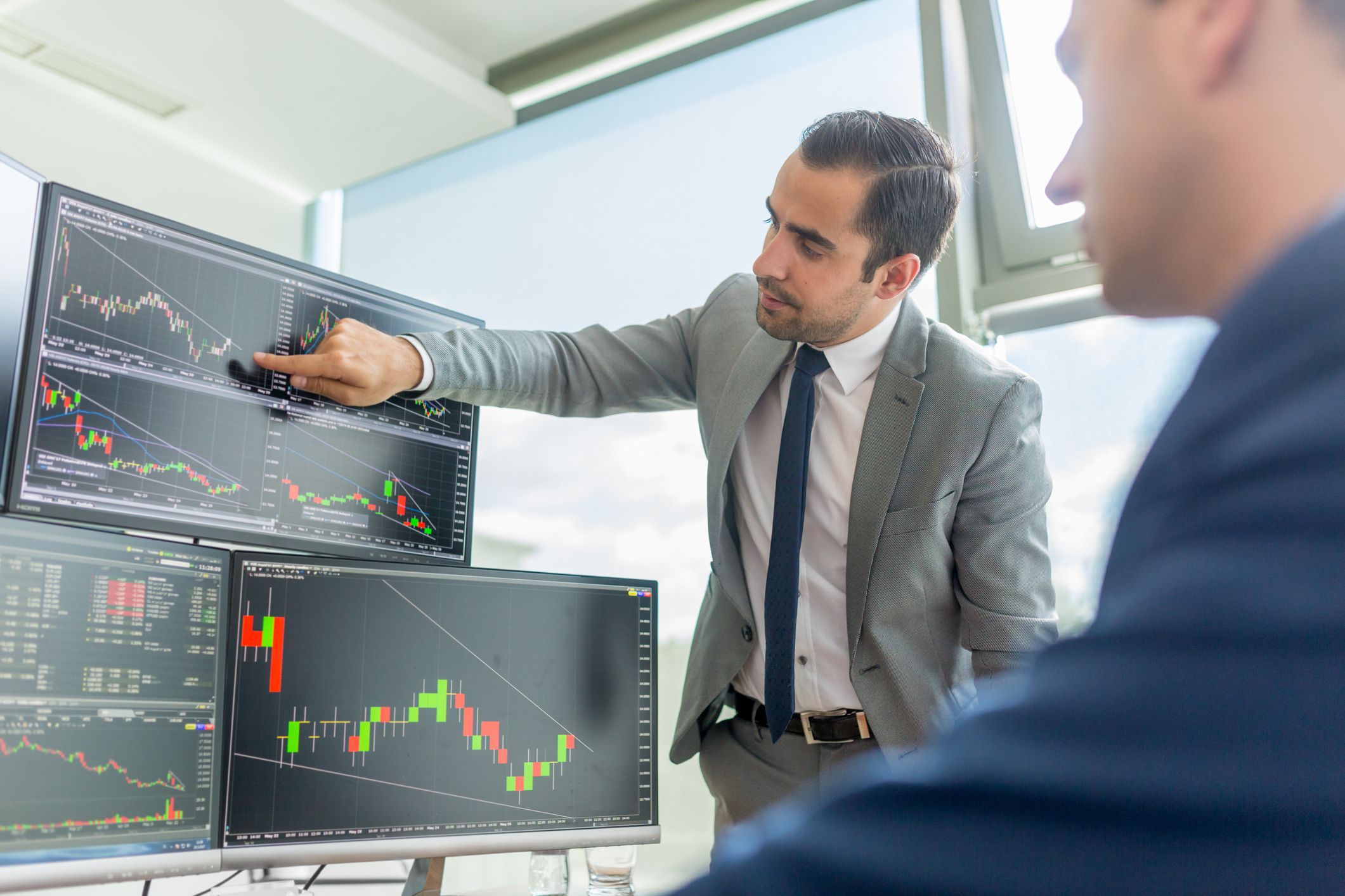 Professional analyzing stock charts on multiple monitors during a market strategy meeting.